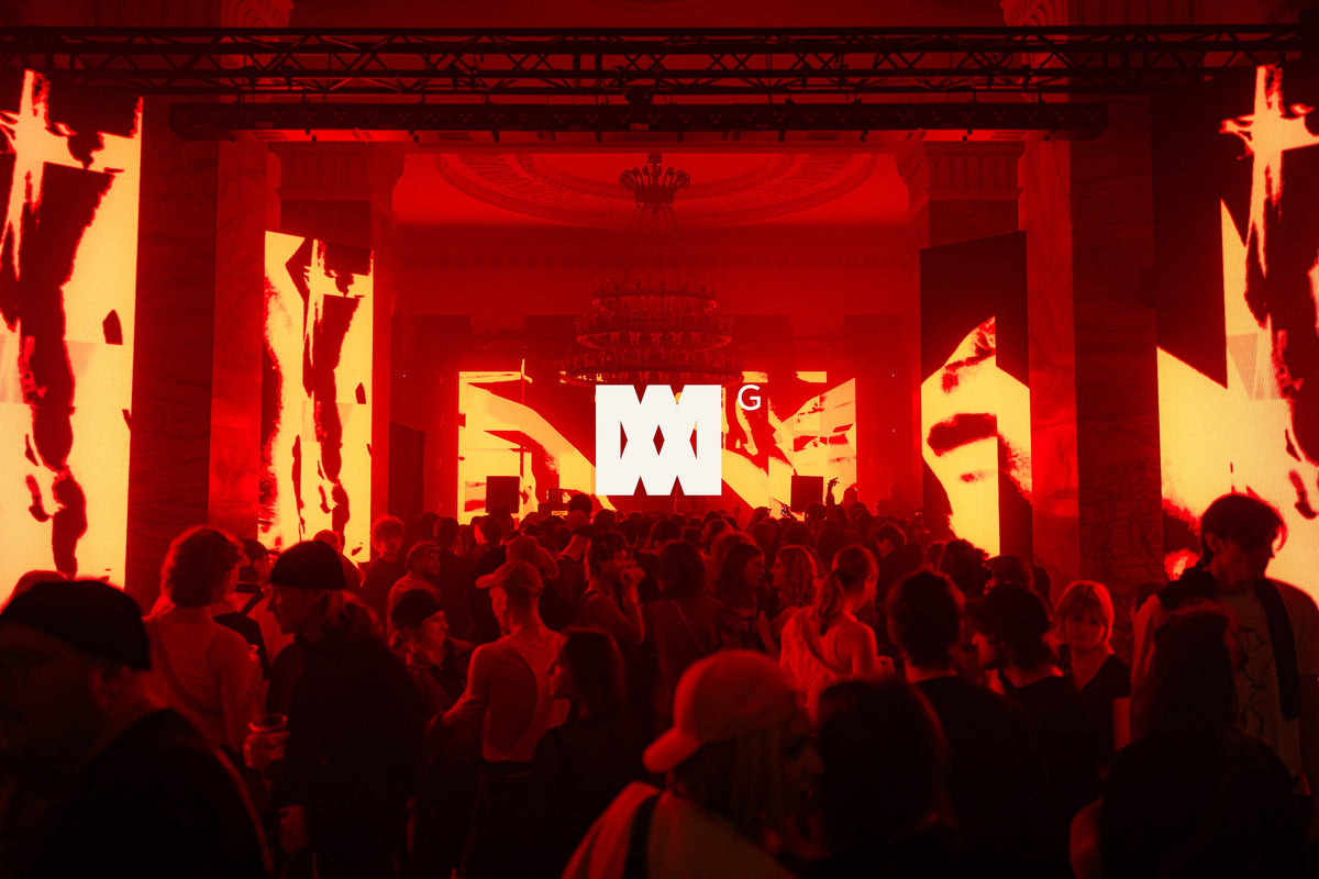 A large crowd gathers inside an elegant event venue, illuminated by vivid red lighting and surrounded by towering LED screens displaying abstract visuals, with the bright white Night Embassy logo at the center of the stage.