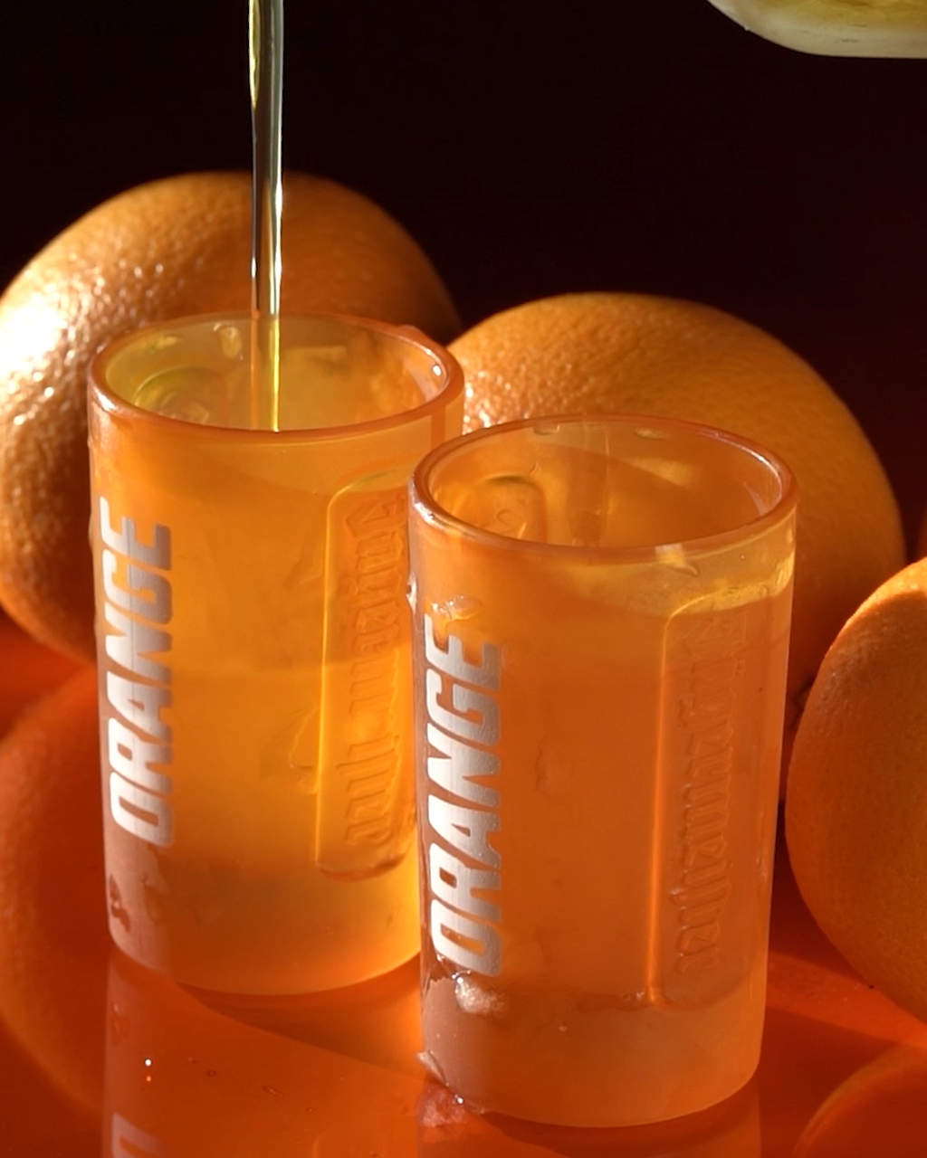 Two orange Jägermeister shot glasses with oranges in the background.