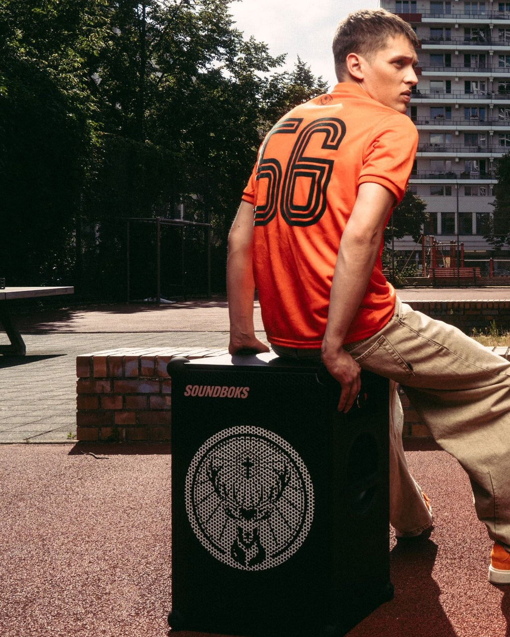 A man in an orange Jägermeister jersey and beige pants sits on a black Soundboks speaker with Jägermeister brand logo